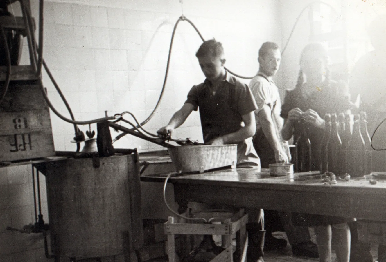 Historische Aufnahme der frühen Saftproduktion: Mitarbeiter füllen an einer kleinen Anlage Fruchtsaft in Bügelflaschen ab.