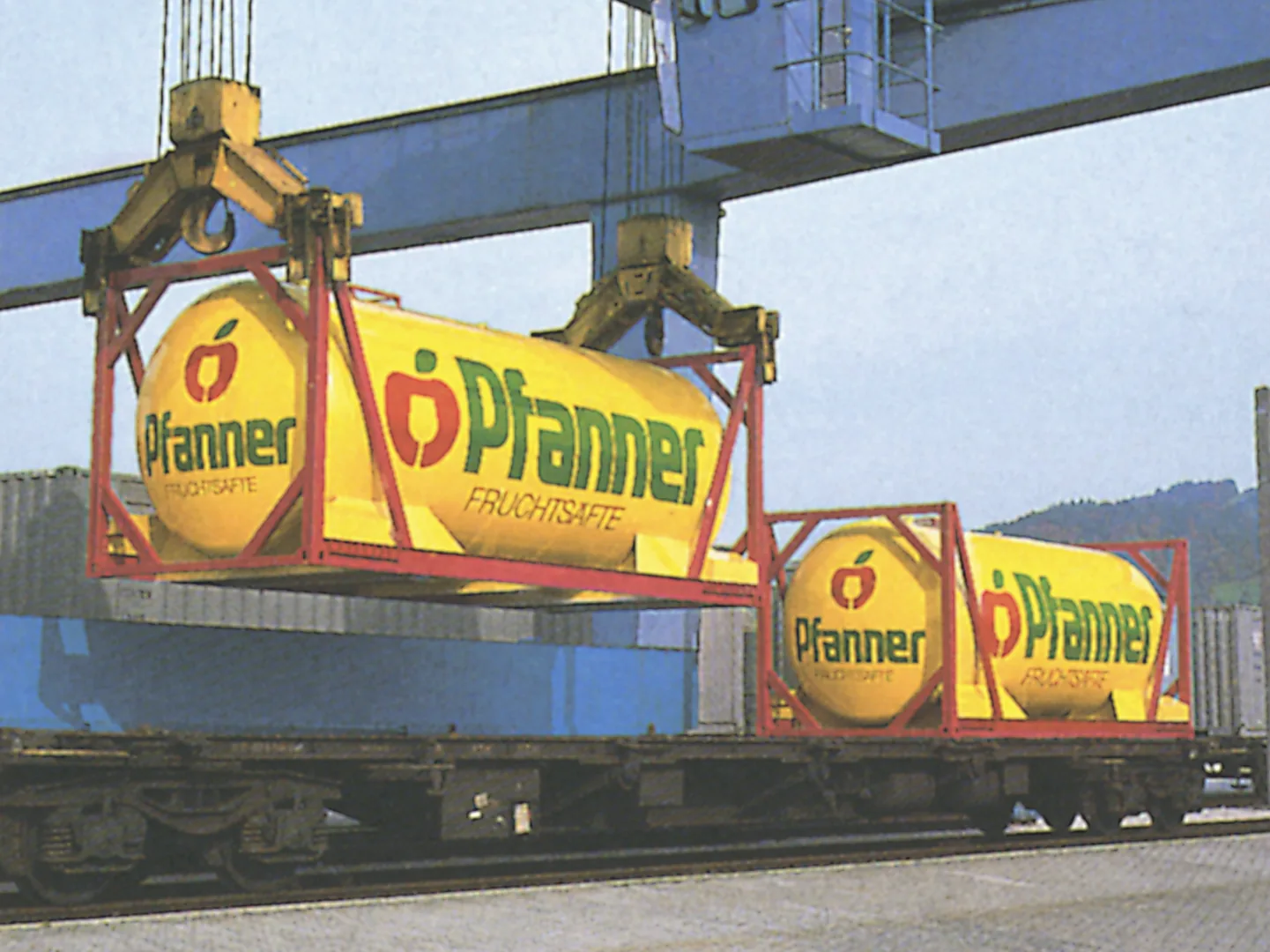 Ein Kran verlädt zwei gelbe Tankcontainer mit Pfanner-Fruchtsäfte-Aufschrift auf einen Eisenbahnwaggon.