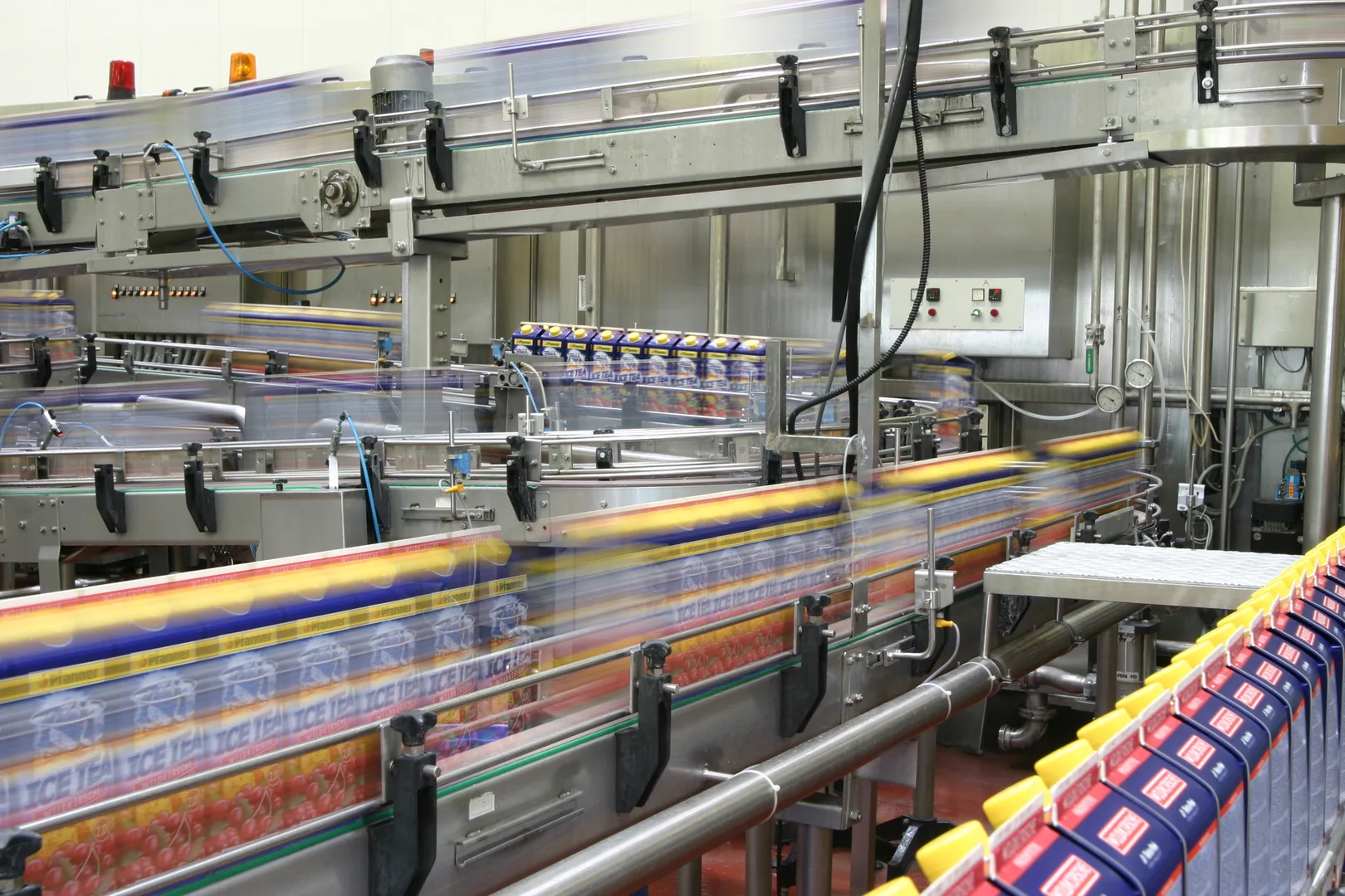 Schnelllaufende Verpackungsanlage mit bewegungsunscharfen Pfanner-Eistee-Kartons auf Edelstahl-Förderbändern.